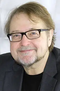 head and shoulders of Urrea with light brown hair, black glasses, with a goatee
