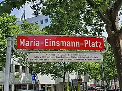 Street sign with white on red text photographed with trees