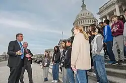 Two older white men in suits address a group of teenagers assembled on the steps of the U.S. Capitol