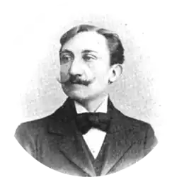 Middle-aged white man with full head of dark hair and pointed moustache