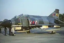 Phantom in grey-green disruptive pattern camouflage. The aircraft has a large red and blue roundel with a red and white checkerboard pattern painted on its air intake, and a phoenix design on its tail.