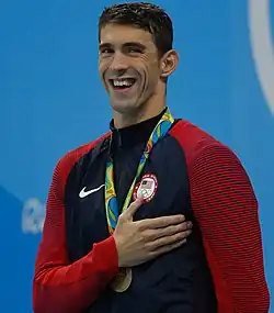 Michael Phelps smiling with his hand over his heart while wearing an Olympic gold medal.