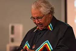 Photo of Justice Murray Sinclair during opening keynote. He is seen, while looking down and smiling, wearing a black top with multi-coloured accents.