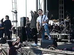 One man playing guitar, one man playing bass guitar, two men singing and one man playing drums on a stage