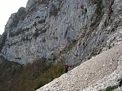 Hiker crossing scree at the foot of a mountain.