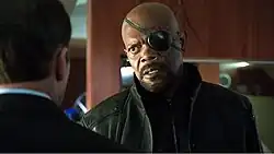 Man with an eye patch over his left eye talking to another man, in an over the shoulder shot