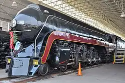 A black streamlined steam locomotive on display with a Christmas wreath hanging in front of it