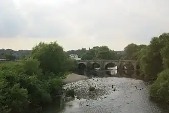 A stone bridge in the centre, trees on either side, and a low flow of water passing through the bridge's arches