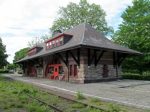 A one-story Richardsonian Romanesque train station next to a disused track
