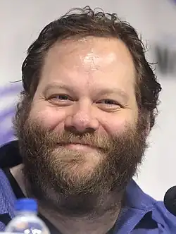 close-up of Ólafur Darri Ólafsson wearing a blue shirt, smiling at the camera, with top of water bottle in foreground