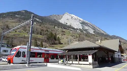 Red-and-white train next to two-story station building