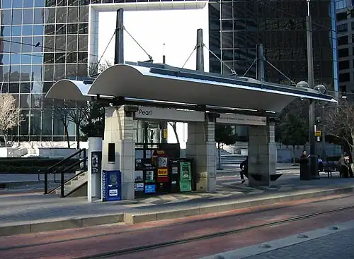Island platform station and canopy in the median of the street with only a few passengers present.