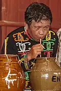 A man in traditional Dusun clothing drinking the tapai with a straw from a jar during Kaamatan