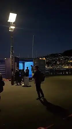 blue light emits from a shipping container with people walking around at night time