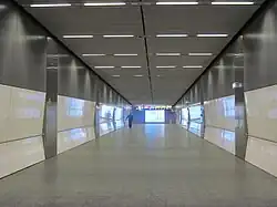 Long and wide pedestrian tunnel with grey tiled floor and white reflective walls