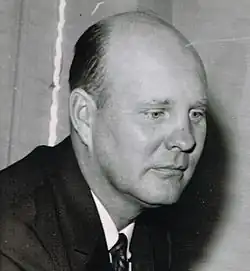 Candid black and white head and shoulders photograph of Ivy wearing a dark suit and looking down slightly