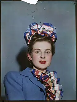 "A busy 1949 city scene in London, England, with black vintage vehicles, red London buses and many pedestrians. Buildings advertise "Wills's Gold Flake Cigarettes" and "Craven A" cigarettes.