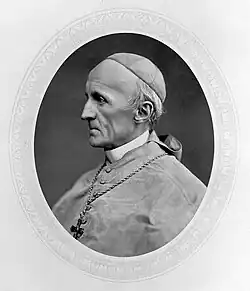 An elderly man wearing a zucchetto, a cross necklace, and a cardinalitial cassock