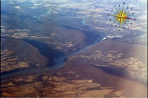Oblique air photo, facing southwest, of the Potomac River flowing through water gaps in the Blue Ridge Mountains. Virginia on the left, Maryland on the right, West Virginia in upper right, including Harpers Ferry (partially obscured by Maryland Heights of Elk Ridge Mountain) at the confluence of the Potomac and Shenandoah Rivers.