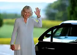 A smiling Camilla waves her hand.