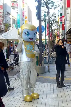 A person in blue, silver, and yellow alien costume waves to onlookers