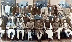 A group photograph of the Rana-Congress coalition cabinet of ministers. Bhadrakali Mishra is seated in the first row, wearing the traditional dhoti-kurta dress and the Gandhian cap. To the right of Mishra is Prime Minister Mohan Shamsher. Also in the photograph are other ministers and other senior administrative and security officials.