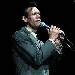 Randy Travis, wearing a gray suit while singing into a microphone