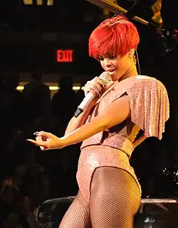 Rihanna, her right hand holding and performing into a microphone, with her left pointing at someone in the crowd