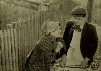 A black and white promotional photograph showing a young man in a vest and a woman in a dark dress standing together