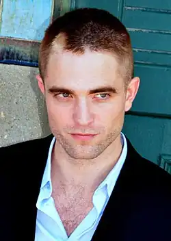 Pattinson with a buzz cut looking to his left with a slight smirk