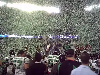 Green and white confetti floats through the air as several players and team staff celebrate a victory.
