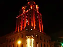 The Elk's Lodge building- which is an Italian Rennisance styled structure is pictured, rising above the street and illuminated with orange light.
