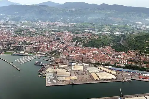 Aerial view of the industrial port and city of Santurtzi with green mountains in the background and ocean in the foreground