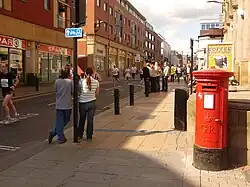 A view looking down Division Street in Sheffield, with a postbox, a Spar shop and pedestrians