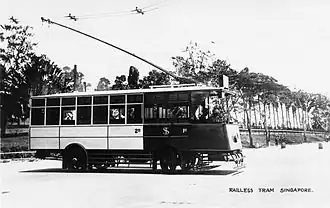 black and white photo showing sideview of an electric tram in Singapore; side is painted to show section for first and second class
