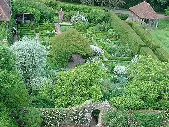 a view of a garden of white flowers with hedging and a boathouse to the right