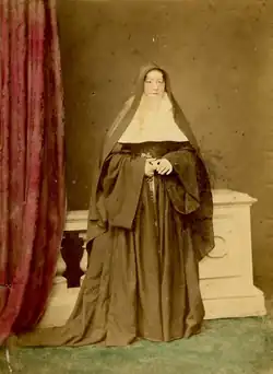 A nun in a big, black and flowing habit standing on green curtain near a fuchsia curtain