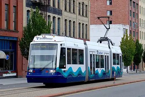 A streetcar traveling in the center of a street, passing several multi-story buildings.