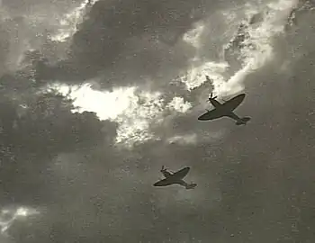 Two Spitfire single-seat piston-engined fighters in flight, silhouetted against cloud