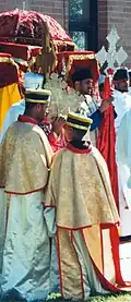 Ethiopian Orthodox clergy lead a procession in celebration of Saint Michael. During such processions, the clergy carry Ethiopian processional crosses and ornately covered tabots around the church building's exterior (Garland, Texas)