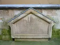 A weathered stone triangular building fragment with a worn carved inscription.