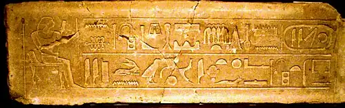 Large block of stone covered with a seated man facing a large hieroglyphic text on its left