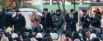 Eight members of Stray Kids talk to each other with mics during a mini fan meeting at the streetwalk.