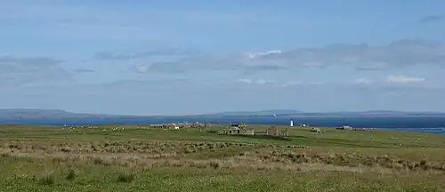 View looking north showing grass fields in the foreground, with ruined buildings visible in the middle distance and sea and islands visible on the horizon