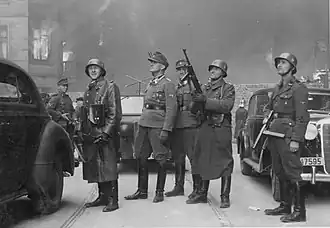 NARA copy #43, IPN copy #43 The leader of the grand operation Second from left Stroop; background either Karl Kaleske&nbsp;[pl] (Stroop's adjutant) or Erich Steidtmann; 2nd from right Heinrich Klaustermeyer; far right Josef Blösche and others at Nowolipie 64 / Smocza 1 intersection