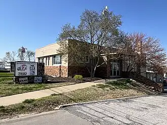 A small office building outside of which is a sign reading "The Networks of Mid Missouri" with the logos of KMIZ, KQFX, KZOU, and Me-TV Mid-Missouri