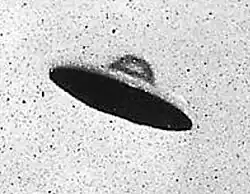 A black and white photo of a blurry, disk shaped aircraft.