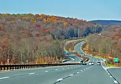 A divided highway in the middle of a late autumn wooded landscape curving up and down through a small valley with hills in the distance