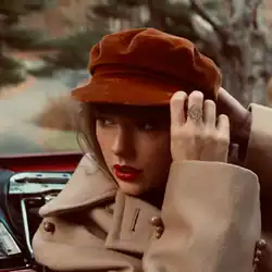 Swift in a red car, wearing a light brown trench coat and a red hat, looking back to the left.