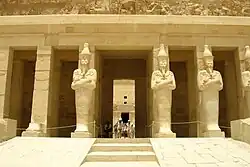 Tall stone statues of Hatshepsut with crossed arms holding a sceptre and a flagellum